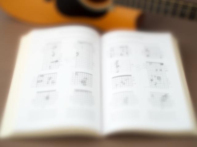 Open textbook showing guitar chord diagrams and finger placements with an acoustic guitar in the background
